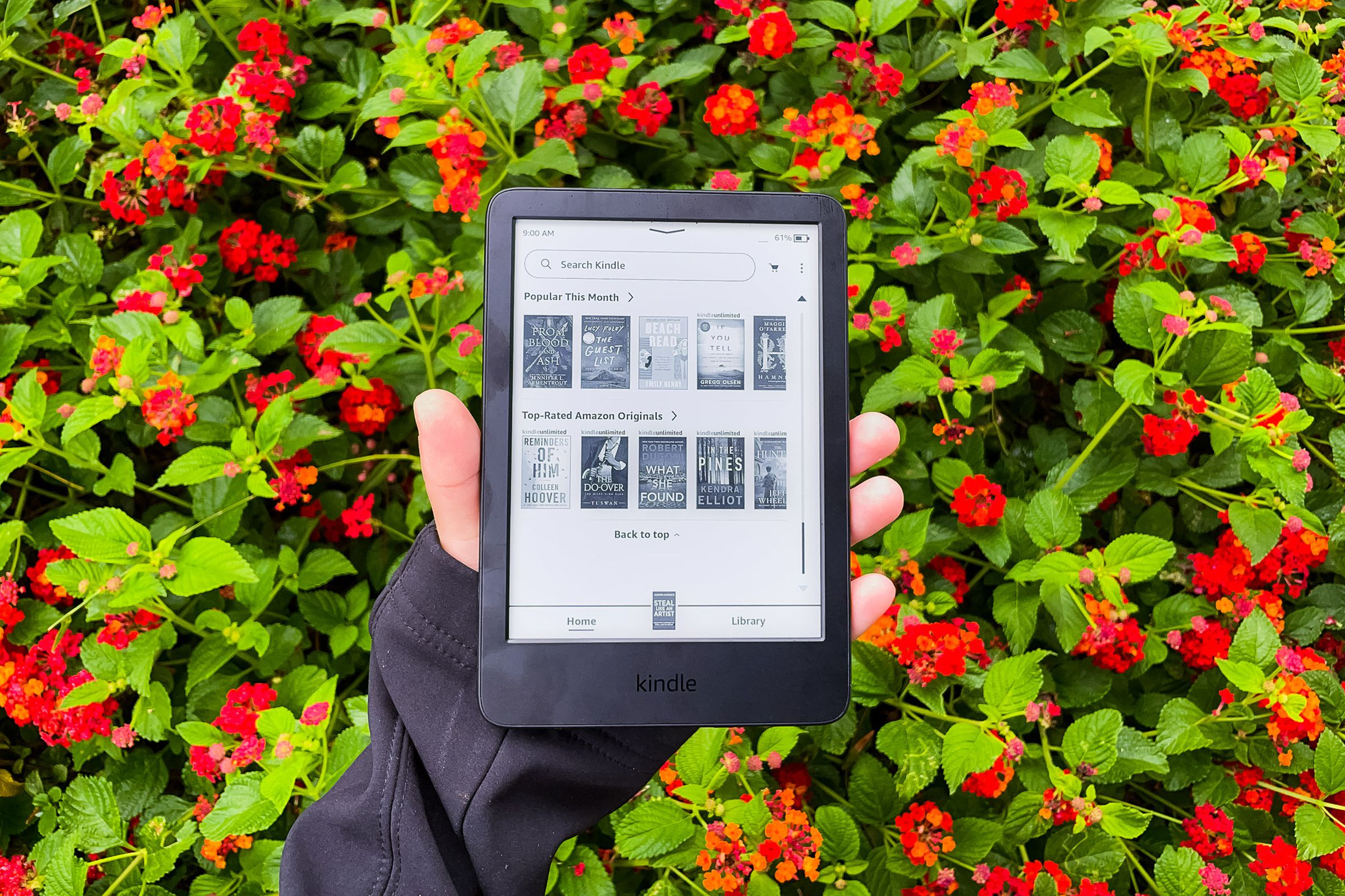 Ένα χέρι που κρατά το Kindle 2022 μπροστά από κόκκινα λουλούδια.