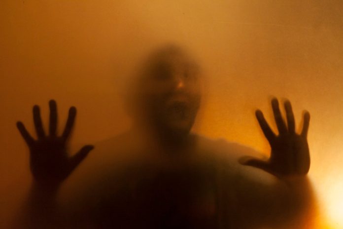 Man screaming with anger behind translucent surface.