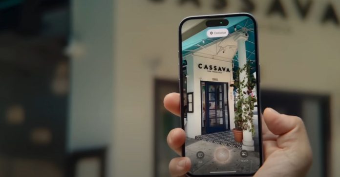 A person using Visual Intelligence from Apple’s iPhone 16 announcement video. The person is holding their iPhone in front of a restaurant and looking at what’s shown onscreen.