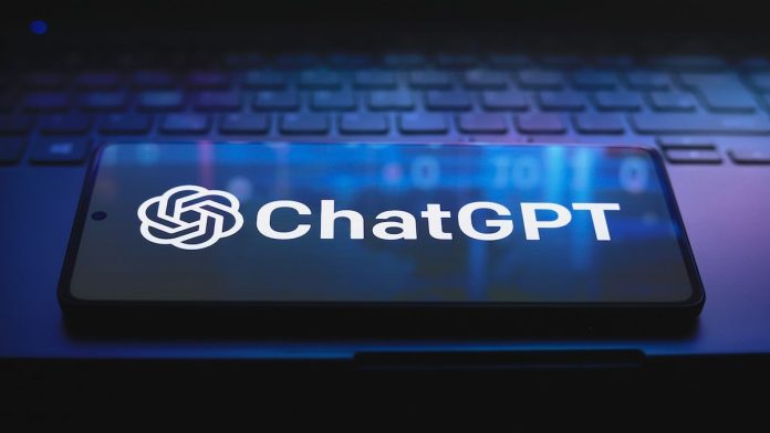 ChatGPT logo on a smart phone resting on a laptop keyboard, lit with a dark purple light