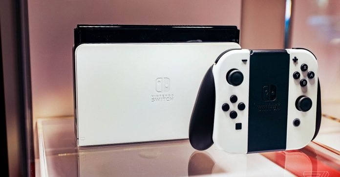 A docked Nintendo Switch OLED model sitting on a piece of glass next to its controller.