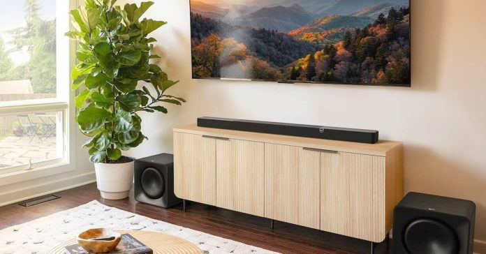 The Klipsch Flexus Core 300 soundbar sitting on a wooden cabinet beneath a wall-mounted TV.