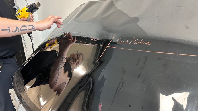 a black car part with a man holding a heat gun. his reflection is seen in the car