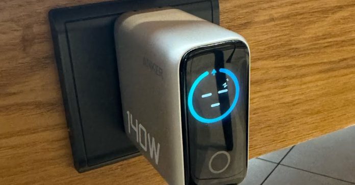 An unreleased Anker wall charger plugged into an outlet with its screen showing a sleeping face.