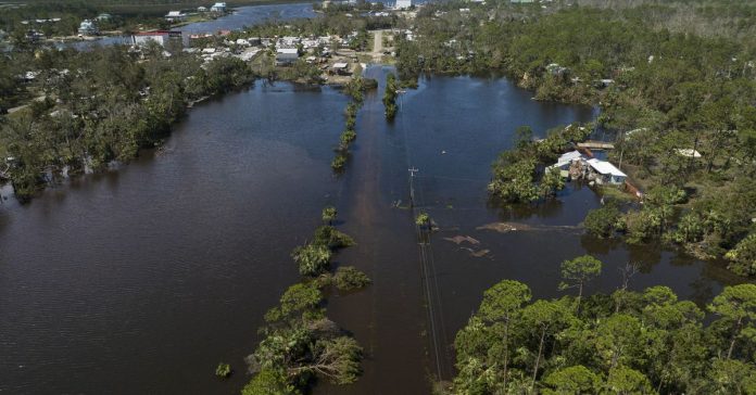 An aerial photo shows a flooded street, with water surrounding structures and trees.